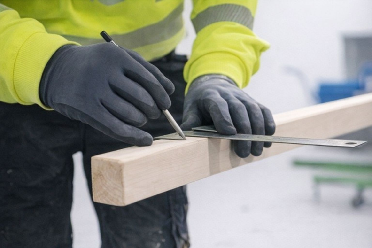En hantverkare i varselkläder mäter och markerar trä för hållbart byggande.